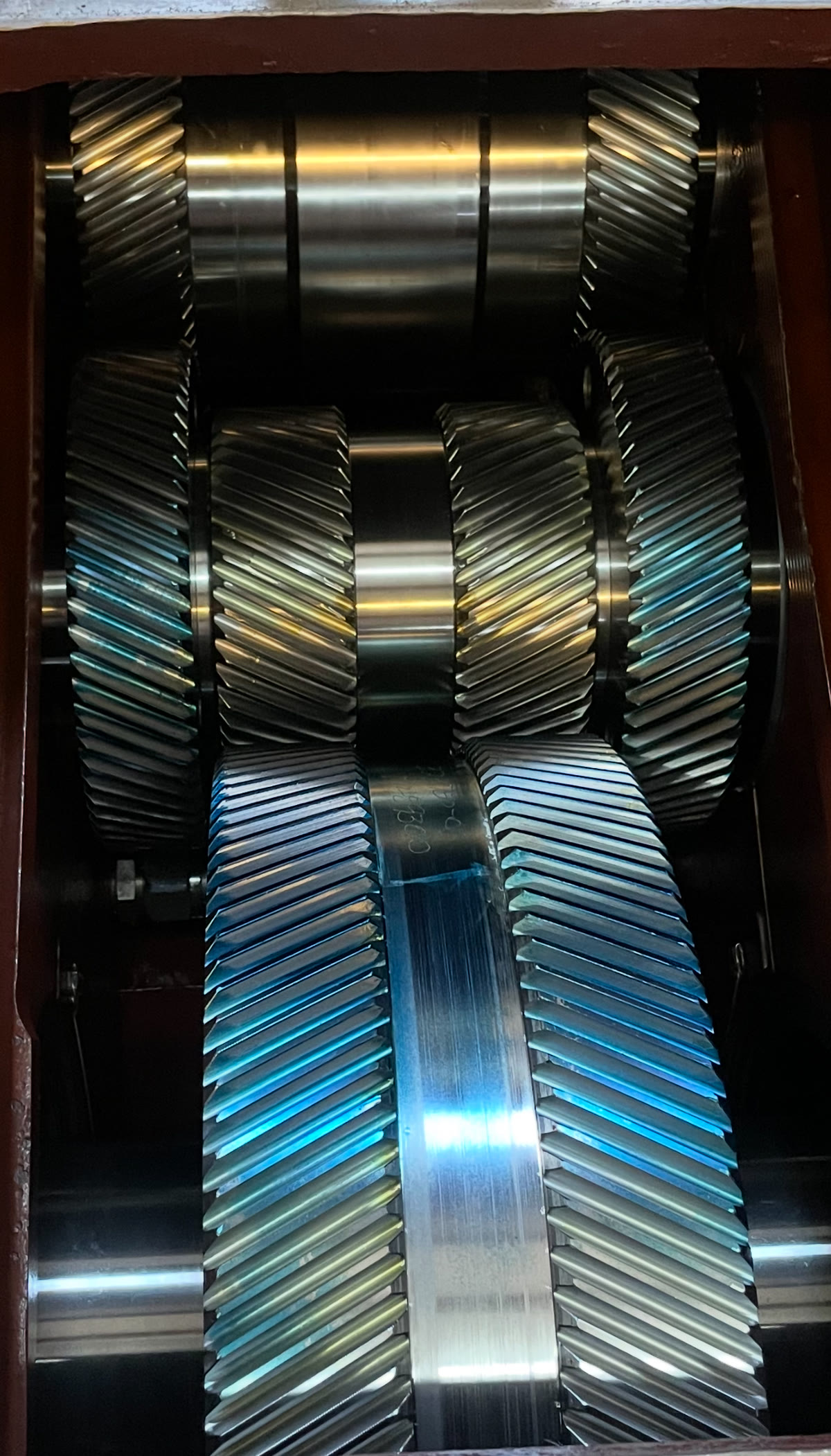 Inside a rebuilt industrial gearbox at Solution Gear Co. in Houston, TX, showing stacked double-helical herringbone gears with a blue heat-tempered finish