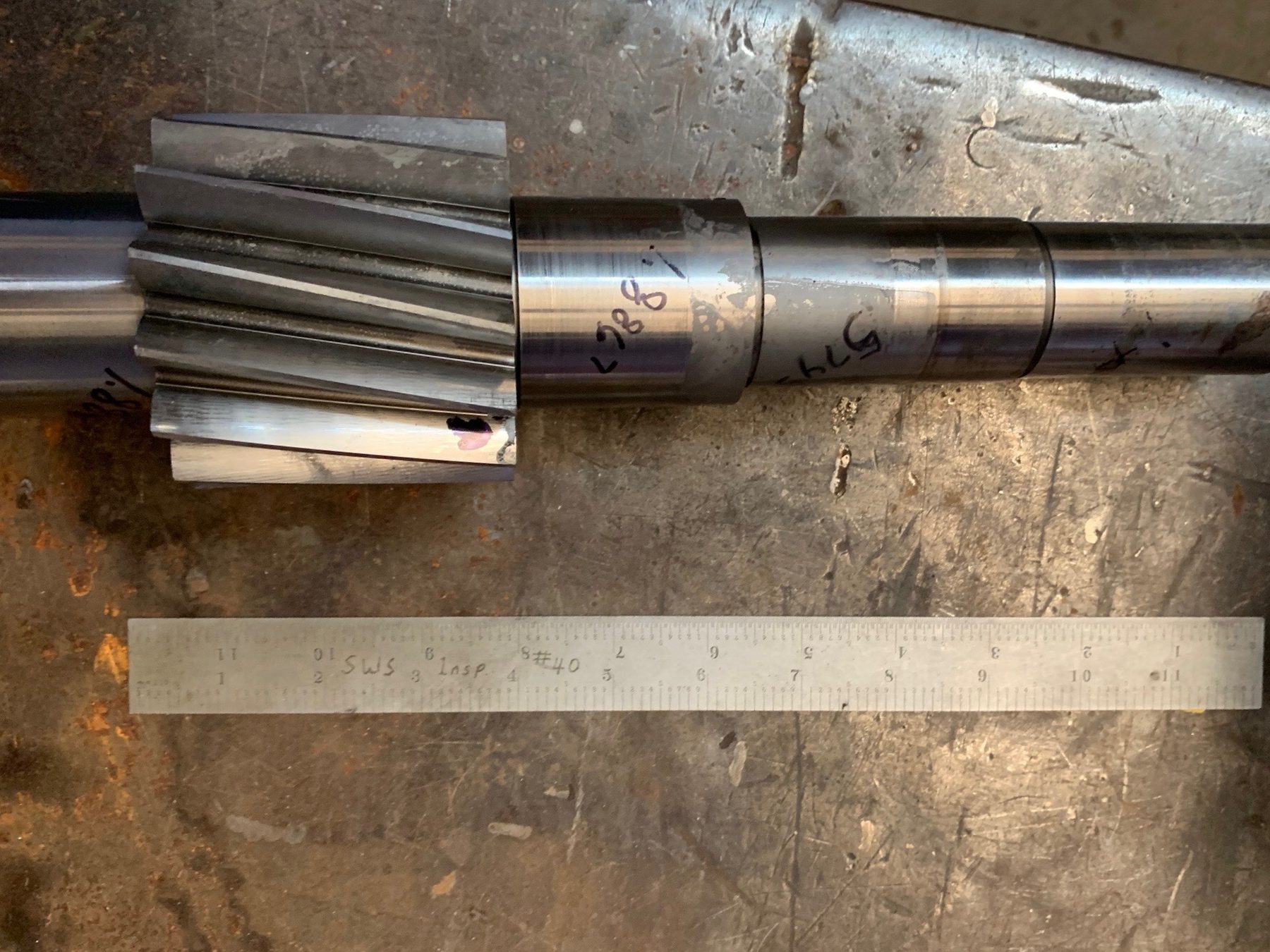 A machined helical pinion gear on its shaft beside a steel rule for inspection